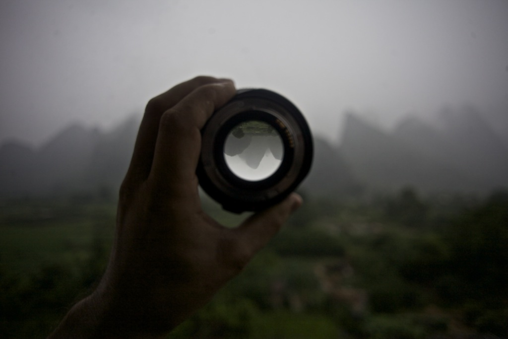 A dark and atmospheric photograph of a lens, through which upside-down mountains are visible