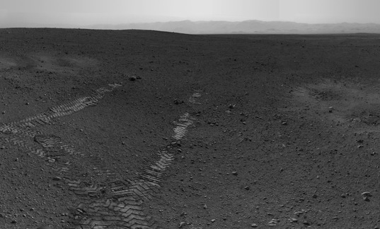 A black and white photograph of tracks leading from nowhere in a desolate landscape, taken on Mars
